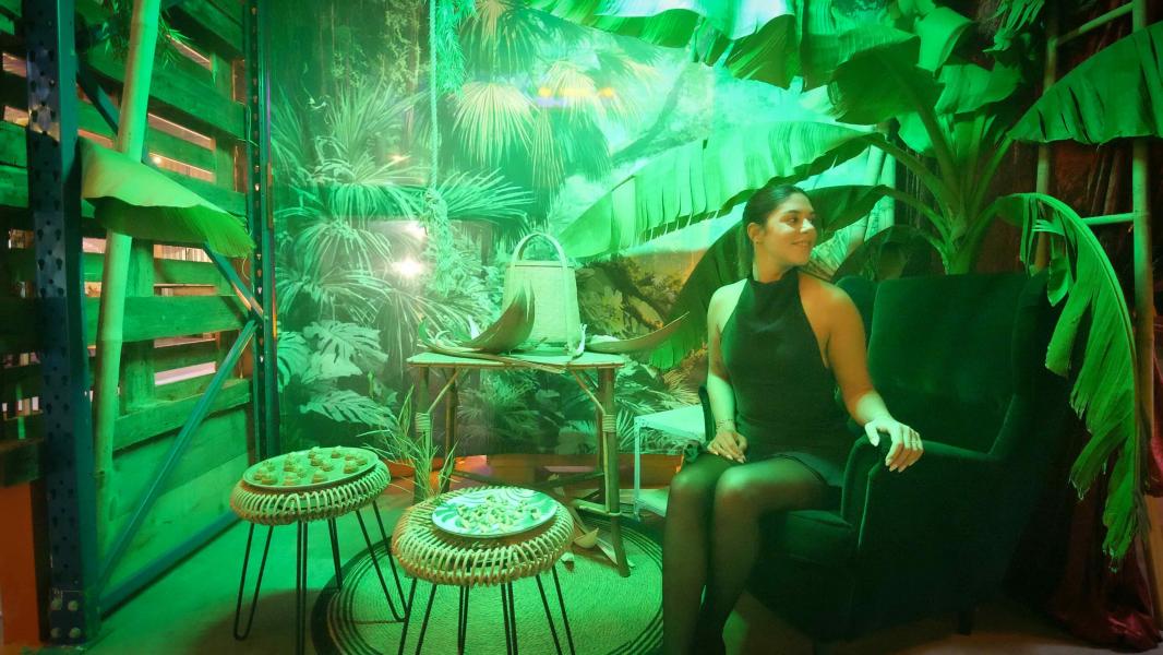 Femme assise devant décor jungle avec lumières vertes et tables de pièces cocktails assorties pour événement thème Jungle Market par Lecointe Stories, organisateur d'événements en Normandie